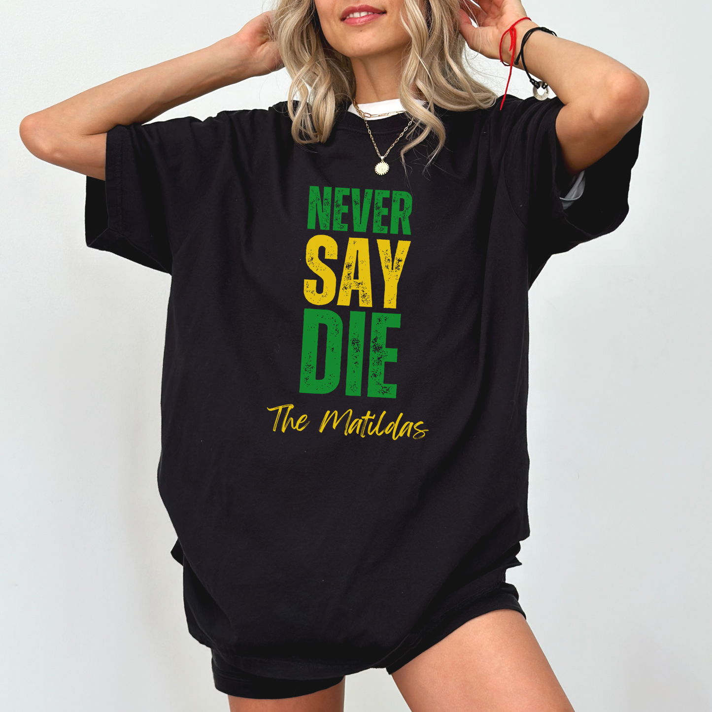 Person wearing a black oversized t-shirt with 'Never Say Die The Matildas' text on a white background