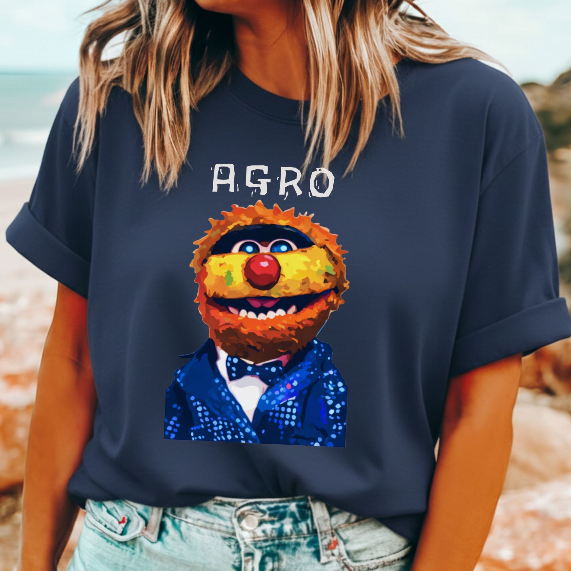 Person wearing a navy blue t-shirt with a colorful character design and 'AGRO' text, standing on a beach.