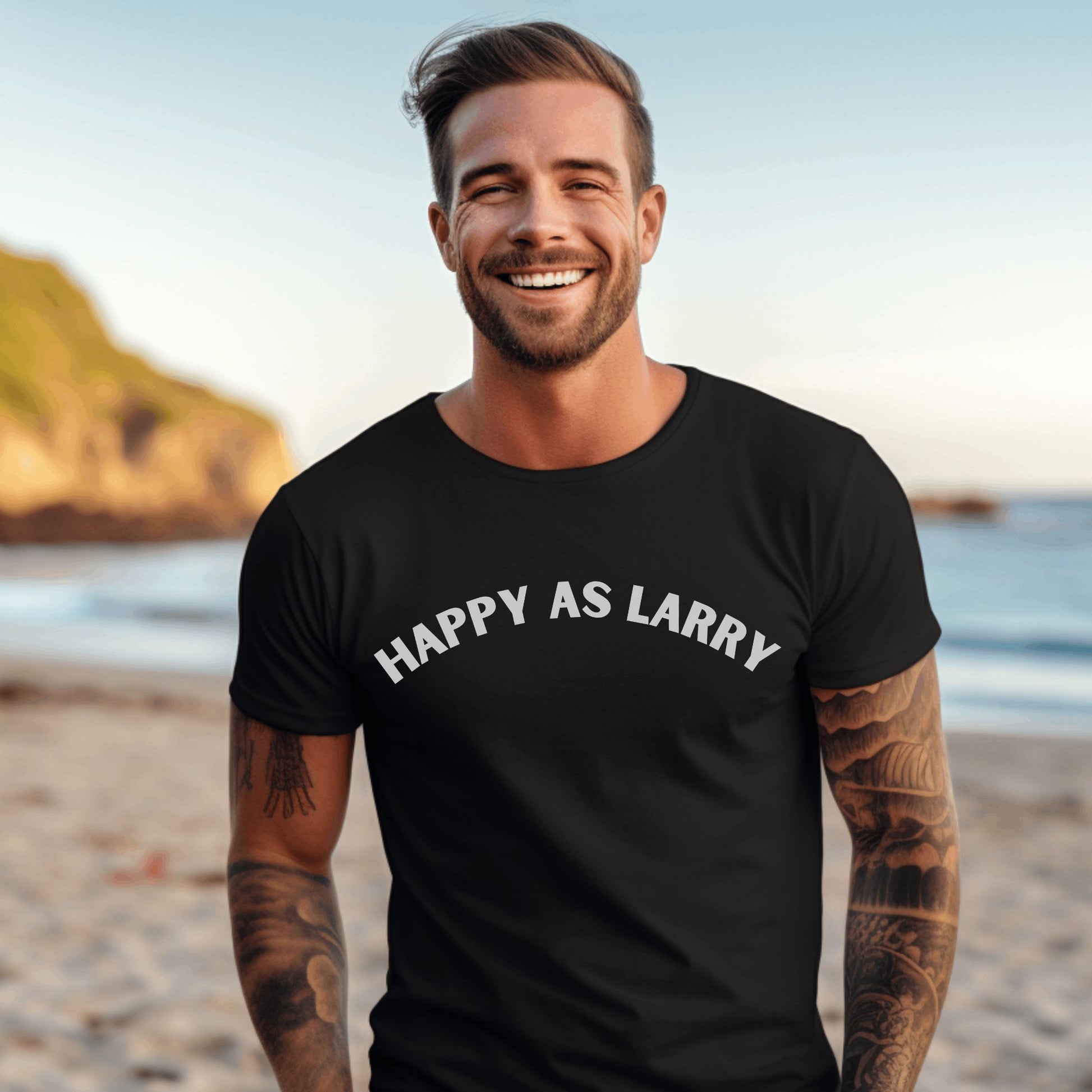 A smiling man with tattoos stands on a beach wearing a black crew-neck t-shirt with the phrase 'HAPPY AS LARRY' printed in white arched text across the chest.