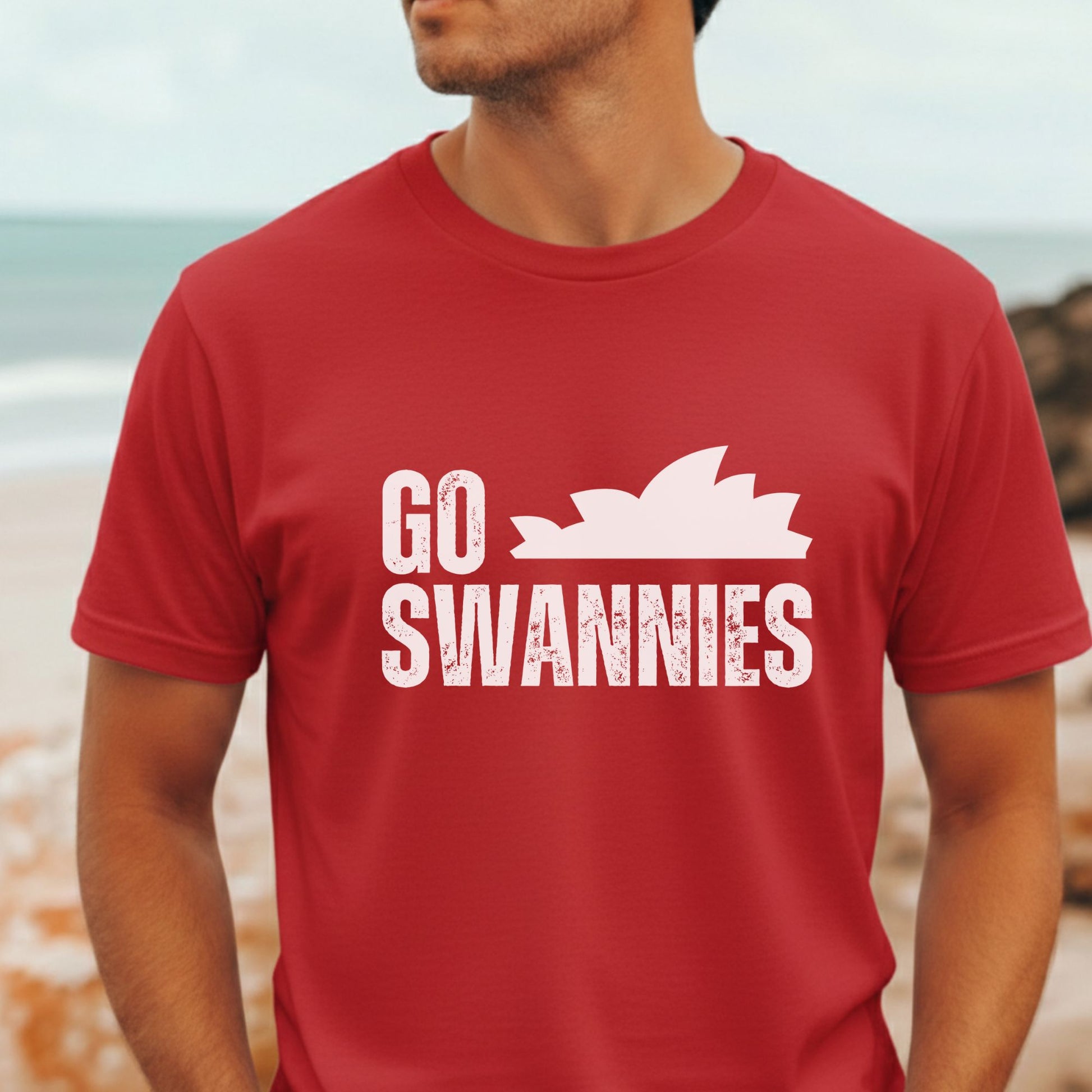 Sydney Swans Red t-shirt with 'GO SWANNIES' and Sydney Opera House graphic on a beach.
